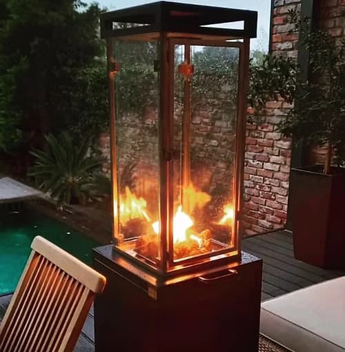 Tall glass-sided gas fire heater burning on a planted terrace