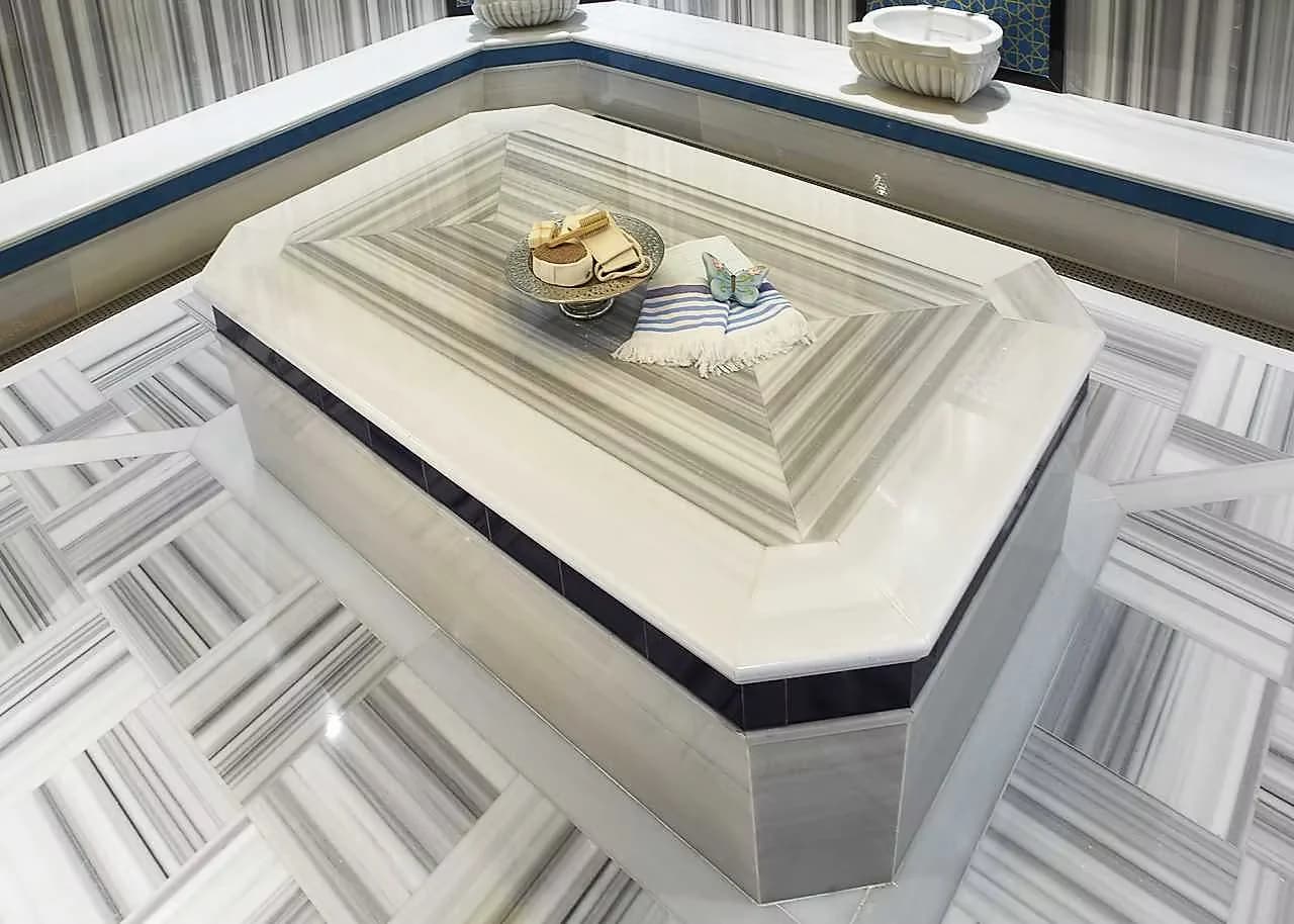 Marble hamam with a heated navel stone at its centre, striped marble floor and folded towels