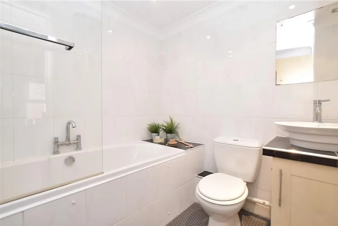Bathroom tiled in white with a bath, screen and wall-hung basin
