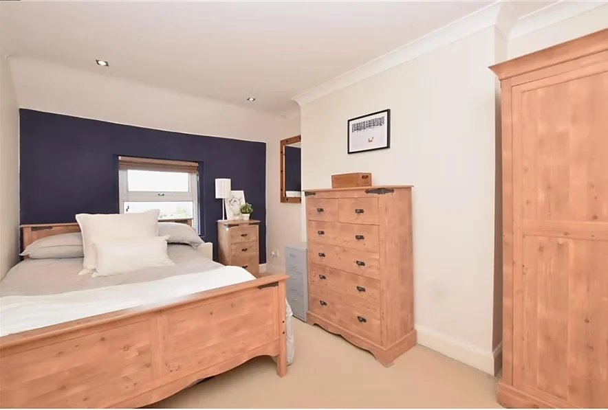 Bedroom with a timber bed and chest of drawers against a dark painted wall