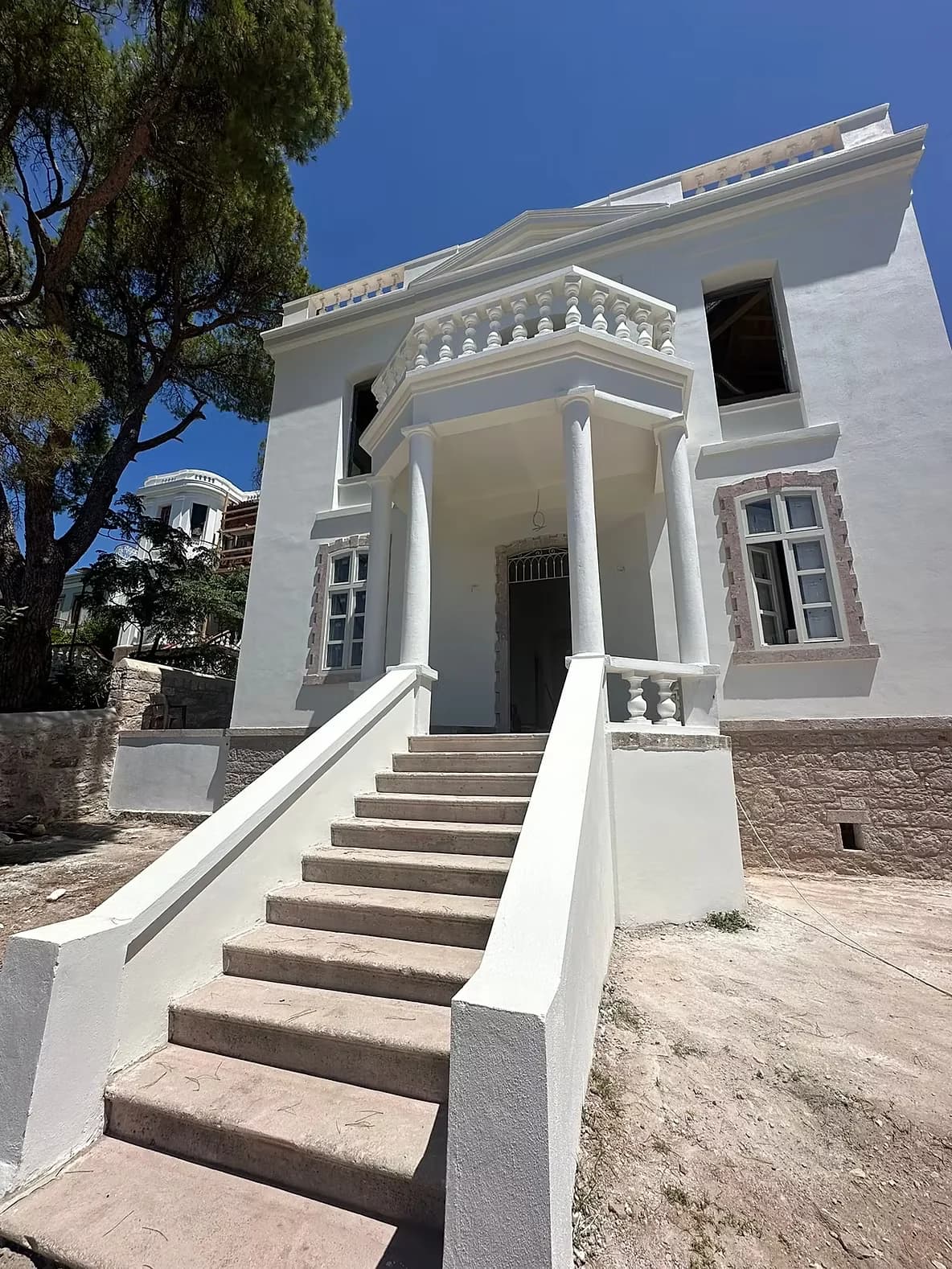The restored house, white render with a columned porch above a stone stair