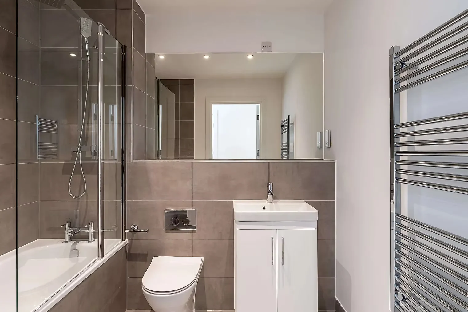 Bathroom tiled floor to ceiling with a mirrored wall above the basin